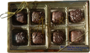 A gold box tied with a ribbon contains eight chocolate-covered caramels sprinkled with sea salt, labeled as "Sugar Free Sea Salt Caramels" from Asher's Chocolate Co.