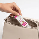 A hand is placing a packet of Nature's Besti sugar replacement into the pocket of a light-colored handbag against a plain background.